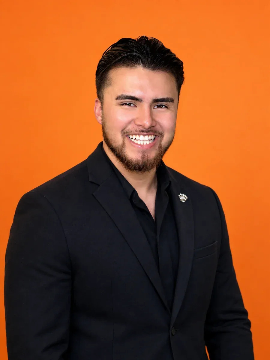 Ulises Herrera, strategy at Zavila Studio, smiling against an orange studio backdrop