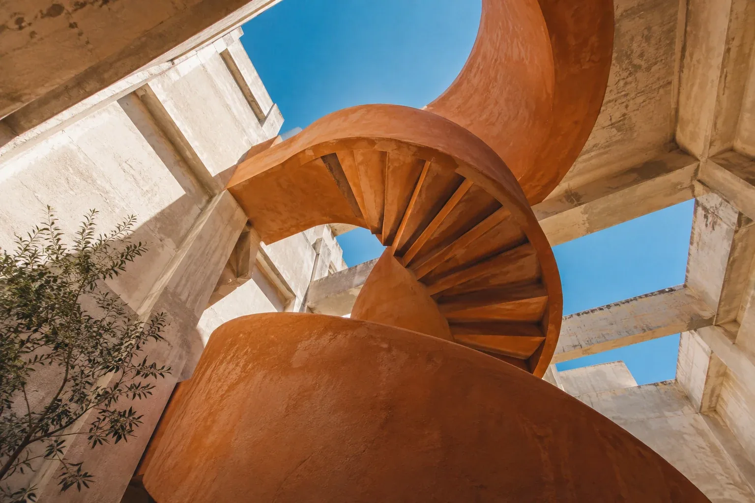 Sculptural terracotta staircase curving through a sunlit concrete building