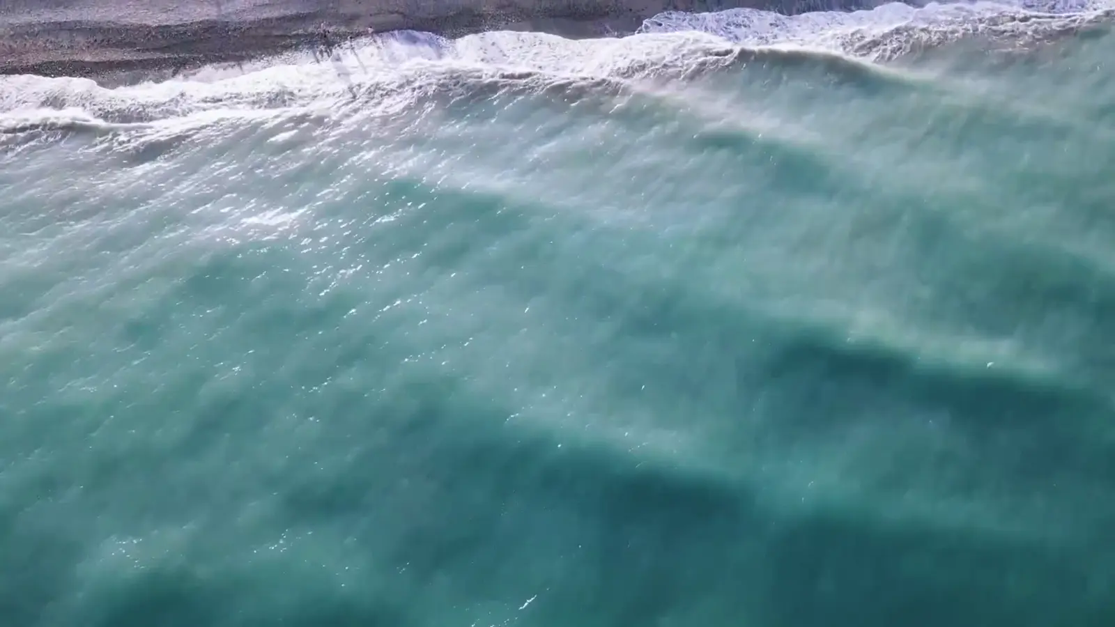 Aerial view of turquoise ocean waves breaking along a rocky shoreline